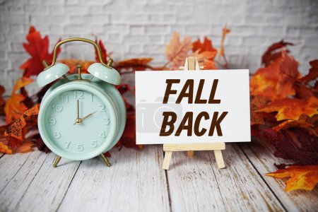 Photo for Fall Back text message with alarm clock and maple leaves on wooden background - Royalty Free Image