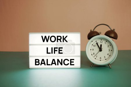 Foto de Mensaje de texto Work Life Balance en tarjeta de papel con caballete de madera y despertador - Imagen libre de derechos