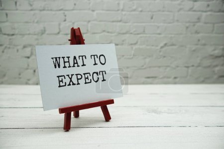 What to Expect? text on white brick wall and wooden background