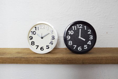 Téléchargez les photos : Horloge alram blanc et noir montrent décalage horaire sur des étagères en bois - en image libre de droit