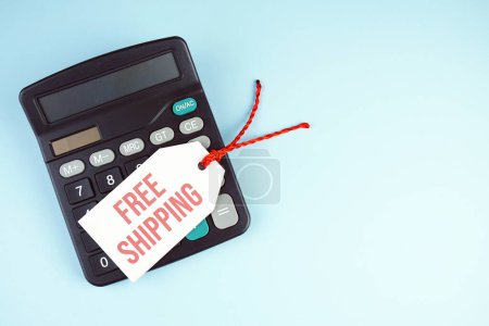 Top view of Free Shipping text on tag sale with calculator flat lay on blue background