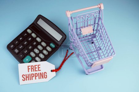 Top view of Free Shipping text on tag sale with calculator and shopping trolly cart flat lay on blue background