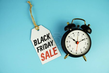 Vista superior del texto de Black Friday Sale en venta con etiqueta con despertador negro plano sobre fondo azul
