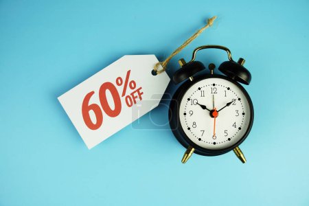 Top view of Sale 60% text on tag sale with black alarm clock flat lay on blue background