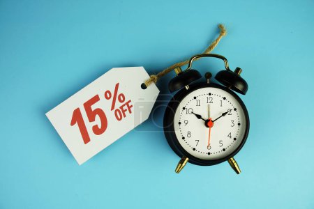 Top view of Sale 15% text on tag sale with black alarm clock flat lay on blue background