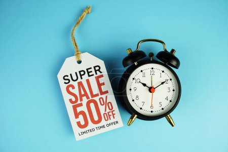 Top view of Super Sale 50% text on tag sale with black alarm clock flat lay on blue background