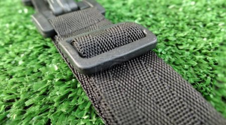 Closeup of black car seat belt on green artificial grass background.