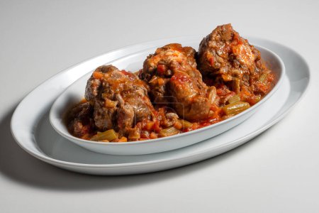 Isolated oval plate with a portion of oxtail stewed vaccinara on white background