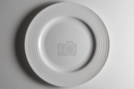 Top view of Empty white dinner plate with edge decorated with concentric circles in relief isolated on white background