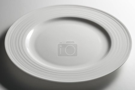 Empty white dinner plate with edge decorated with concentric circles in relief isolated on white background