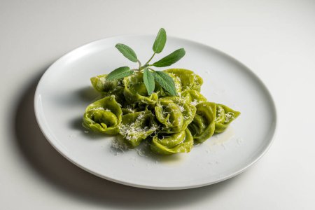 Dinner plate of green ravioli with sage and parmesan on white background