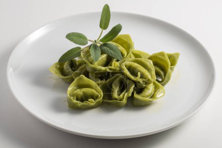Dinner plate with green ravioli and sage on white background