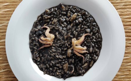 Top view of Dish with risotto and squid ink on straw background