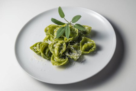 Speiseteller mit grünen Ravioli mit Salbei und Parmesan auf weißem Hintergrund