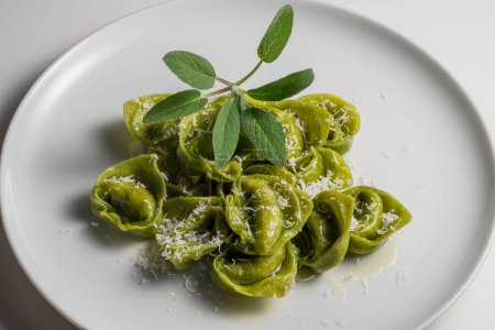 Detail of Dinner plate of green ravioli with sage and parmesan on white background
