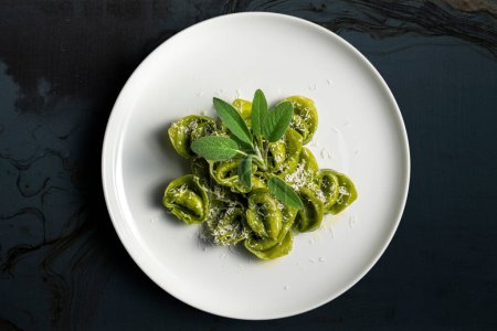 Top view of Dinner plate of green ravioli with sage and parmesan on dark background