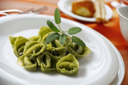 Dinner plate with green ravioli and sage on a laid table