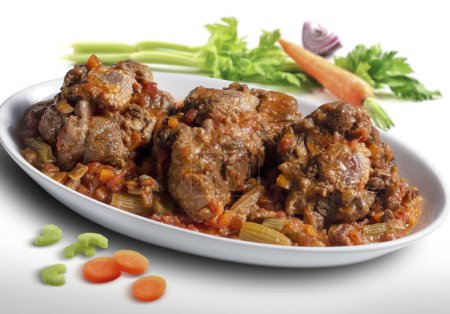 Isolated oval plate with a portion of oxtail stewed vaccinara and vegetables on white background