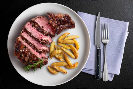 Vue du dessus de l'assiette avec steak de boeuf et pommes de terre sur ardoise noire avec serviette et couverts