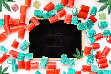 Cannabis products flat lay buds and gummy candies on chalk board with copy space