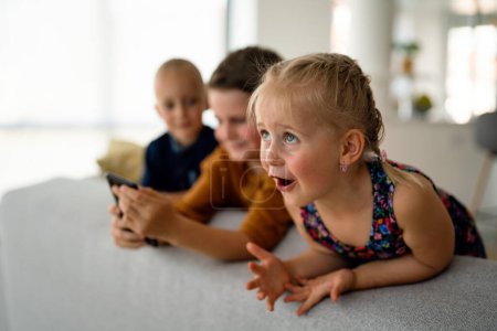 Téléchargez les photos : Portrait d'enfants s'amusant, jouant sur un téléphone portable ensemble à la maison. Internet et dépendance au réseau. - en image libre de droit