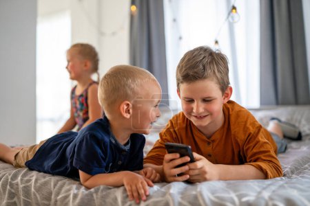Photo for Portrait of children having fun, playing on mobile phone together at home. Internet and network addiction. - Royalty Free Image