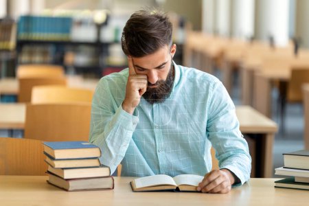 Foto de Hombre cansado joven cansado estudiando y preparándose para el examen en la biblioteca de la universidad. Concepto gente educación - Imagen libre de derechos
