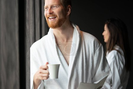 Téléchargez les photos : Jeune homme en peignoir buvant du café à l'hôtel, centre spa. - en image libre de droit