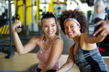 Photo for Happy fit women, friends smiling, talking and taking photos after work out in gym. Social media, people, sport concept. - Royalty Free Image