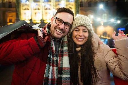Téléchargez les photos : Portrait de couple souriant heureux avec des cadeaux de Noël dans la ville. Shopping gens concept de vente - en image libre de droit