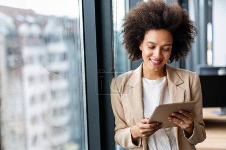 Téléchargez les photos : Portrait d'une jeune femme d'affaires afro-américaine confiante et souriante travaillant avec une tablette numérique au bureau - en image libre de droit