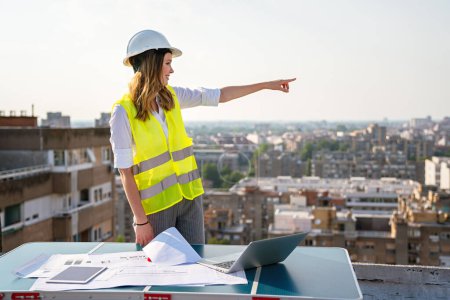 Photo for Young successful woman construction specialist architect reviewing blueprints at construction site - Royalty Free Image