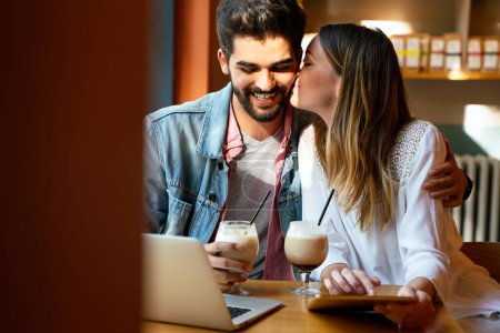 Foto de Feliz joven pareja sentada en la cafetería sonriendo, mirando a la pantalla del ordenador portátil, pasar tiempo con placer, beber café. - Imagen libre de derechos