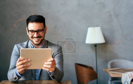 Téléchargez les photos : Jeune homme d'affaires prospère souriant, entrepreneur dans une suite d'affaires formelle travaillant sur tablette numérique - en image libre de droit