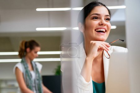 Téléchargez les photos : Succès jeune femme d'affaires d'entreprise travaillant sur ordinateur portable dans le bureau avec des collègues à l'arrière-plan. - en image libre de droit