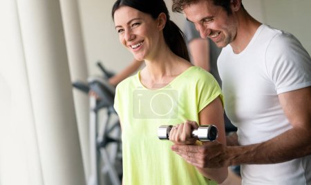 Photo for Handsome man trainer flirting with beautiful young woman while helping her at gym - Royalty Free Image
