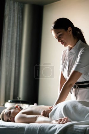 Téléchargez les photos : Masseur faisant massage sur le corps de la jeune femme dans le salon de spa - en image libre de droit