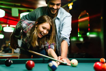 Foto de Feliz joven sonriente pareja disfrutando jugando al billar en el bar. Gente entretenimiento divertido concepto - Imagen libre de derechos