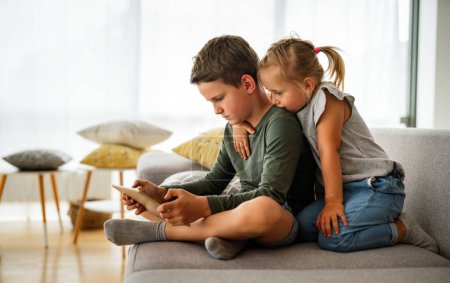 Téléchargez les photos : Petite fille et garçon regardant des vidéos ou jouant à des jeux sur leur tablette d'appareil numérique, smartphone. Concept de dépendance numérique des enfants. - en image libre de droit