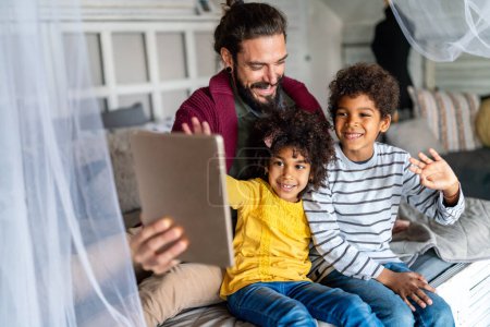 Téléchargez les photos : Père heureux et les enfants en utilisant une tablette numérique et s'amuser à la maison. Concept de bonheur familial multiethnique - en image libre de droit