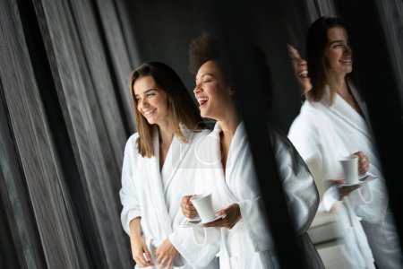 Photo for Lesbian couple women relaxing and drinking tea in robes during wellness - Royalty Free Image