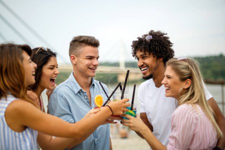 Foto de Grupo de amigos felices divirtiéndose en fiesta en la playa bebiendo cóctel al atardecer. Alegría de verano y concepto de amistad con los jóvenes de vacaciones - Imagen libre de derechos