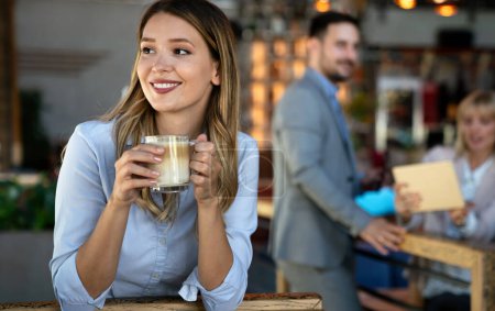 Photo for Portrait of happy young successful business woman drinking coffee in a break. In the background, her colleagues - Royalty Free Image