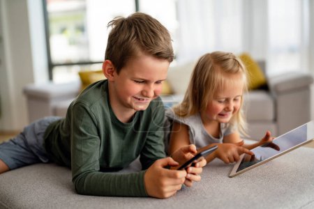 Téléchargez les photos : Petite fille et garçon regardant des vidéos ou jouant à des jeux sur leur tablette d'appareil numérique, smartphone. Concept de dépendance numérique des enfants. - en image libre de droit