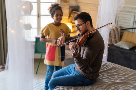 Photo for Single father and adopted daughter playing on instrument together. Adult man playing violin for child girl. - Royalty Free Image