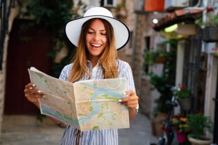 Photo for Young happy woman tourist with map looking for a way on summer vacation - Royalty Free Image