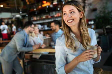Téléchargez les photos : Portrait d'une jeune femme d'affaires heureuse et prospère qui boit du café pendant une pause. En arrière-plan, ses collègues - en image libre de droit