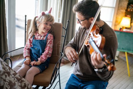 Téléchargez les photos : Bonne famille. Père et fille jouent de l'instrument ensemble. Homme adulte jouant du violon pour enfant fille. - en image libre de droit