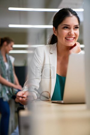 Foto de Éxito joven mujer de negocios corporativos que trabajan en el ordenador portátil en la oficina con colegas en el fondo. - Imagen libre de derechos