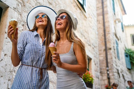 Photo for Laughing girls friends eating ice cream cones enjoying their summer vacation. Travel people fun concept. - Royalty Free Image